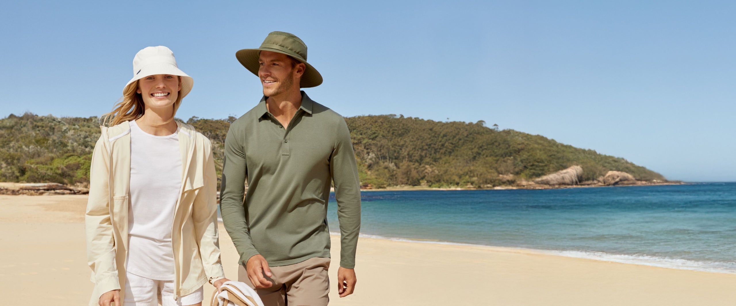 Man and woman walking on a beach with a clear blue sky and ocean in the background