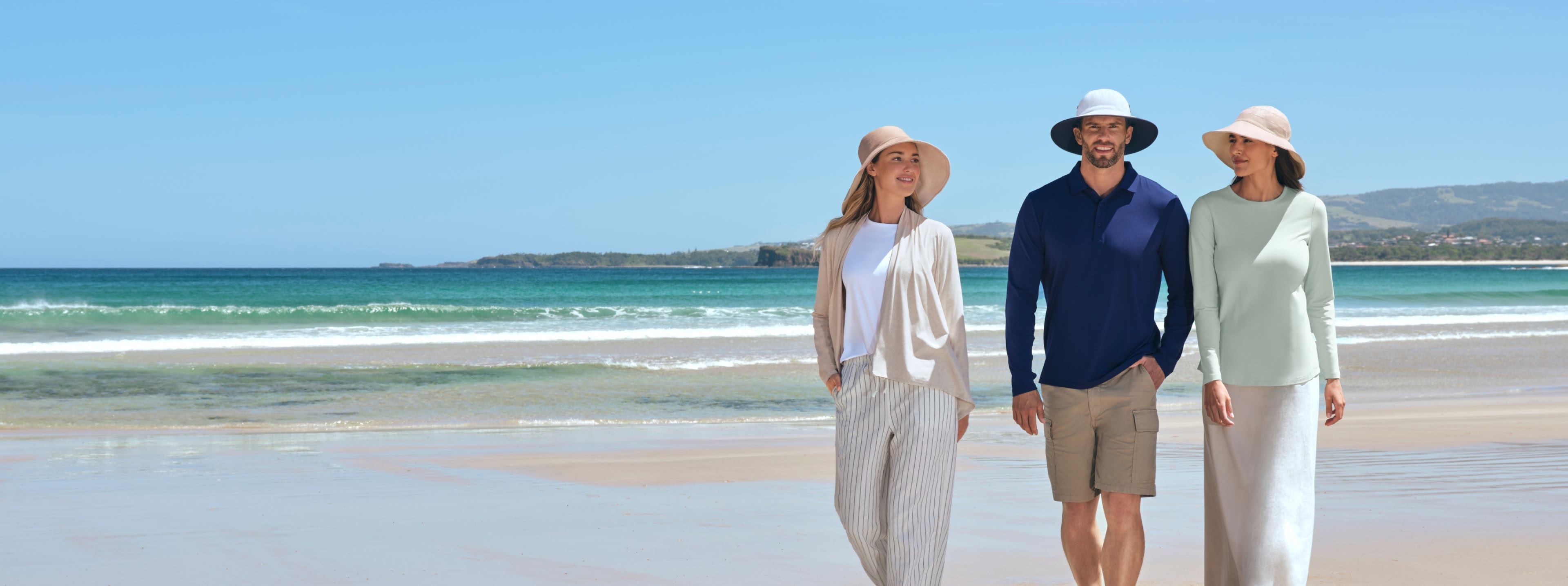 Three people standing on a beach with clear blue sky and ocean.