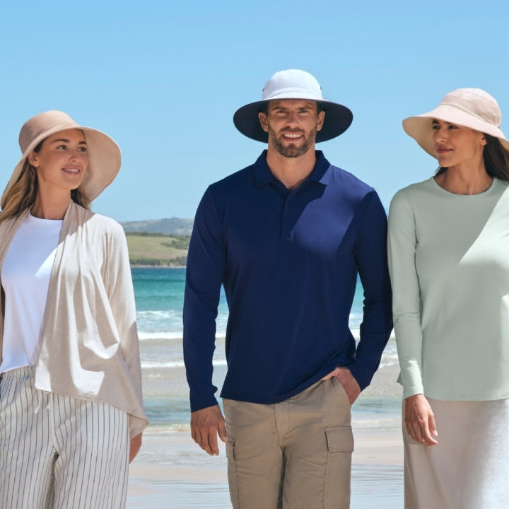 Three people standing on a beach wearing UPF 50+ clothing and hats.