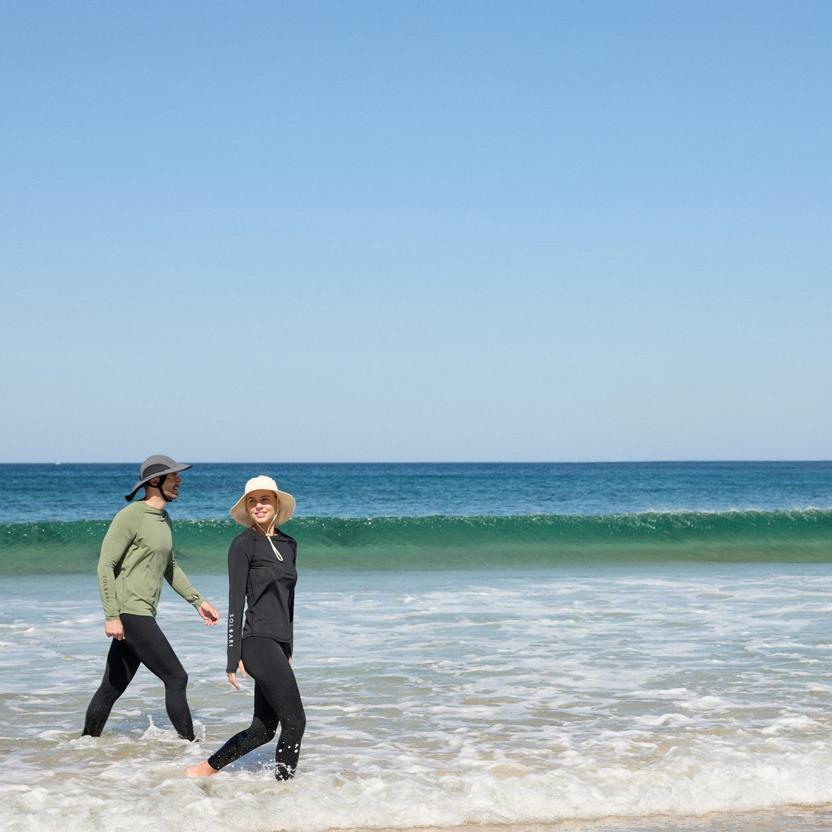 Two people walking on a beach with clear blue sky and ocean.