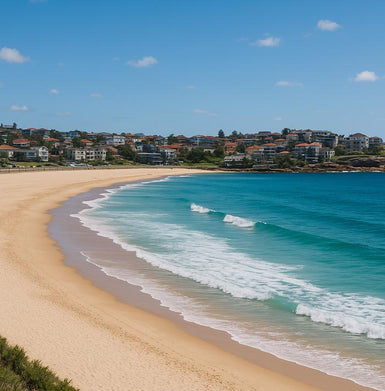 Beach scene with clear blue sky, turquoise water, and houses in the background.
